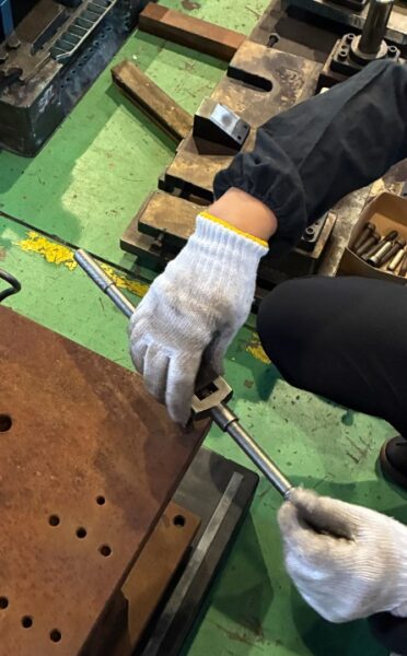 金型メンテナンスのため作業者がタップハンドルを使い、錆びたプレス金型の吊りボルト用ネジ穴を整えている様子