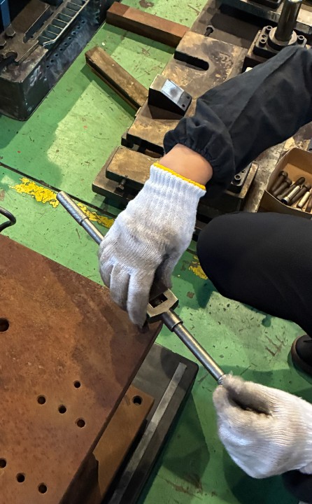 作業者がタップハンドルを使い、錆びたプレス金型の吊りボルト用ネジ穴を整えている様子