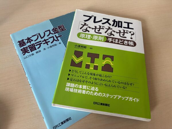 2冊の本の写真。「基本プレス金型 実習テキスト」および『プレス加工「なぜなぜ?」原理・原則手ほどき帳』」が写っている。