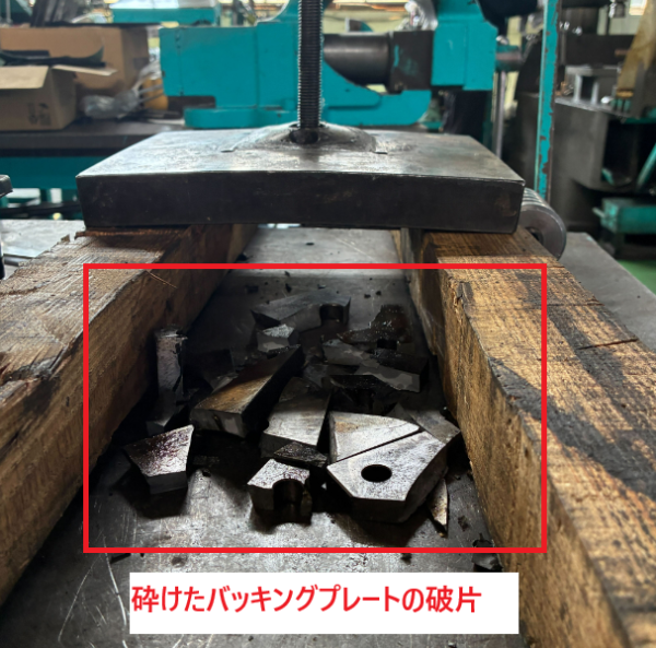 プレス金型の下部に粉砕されたバッキングプレートの破片が散乱している様子